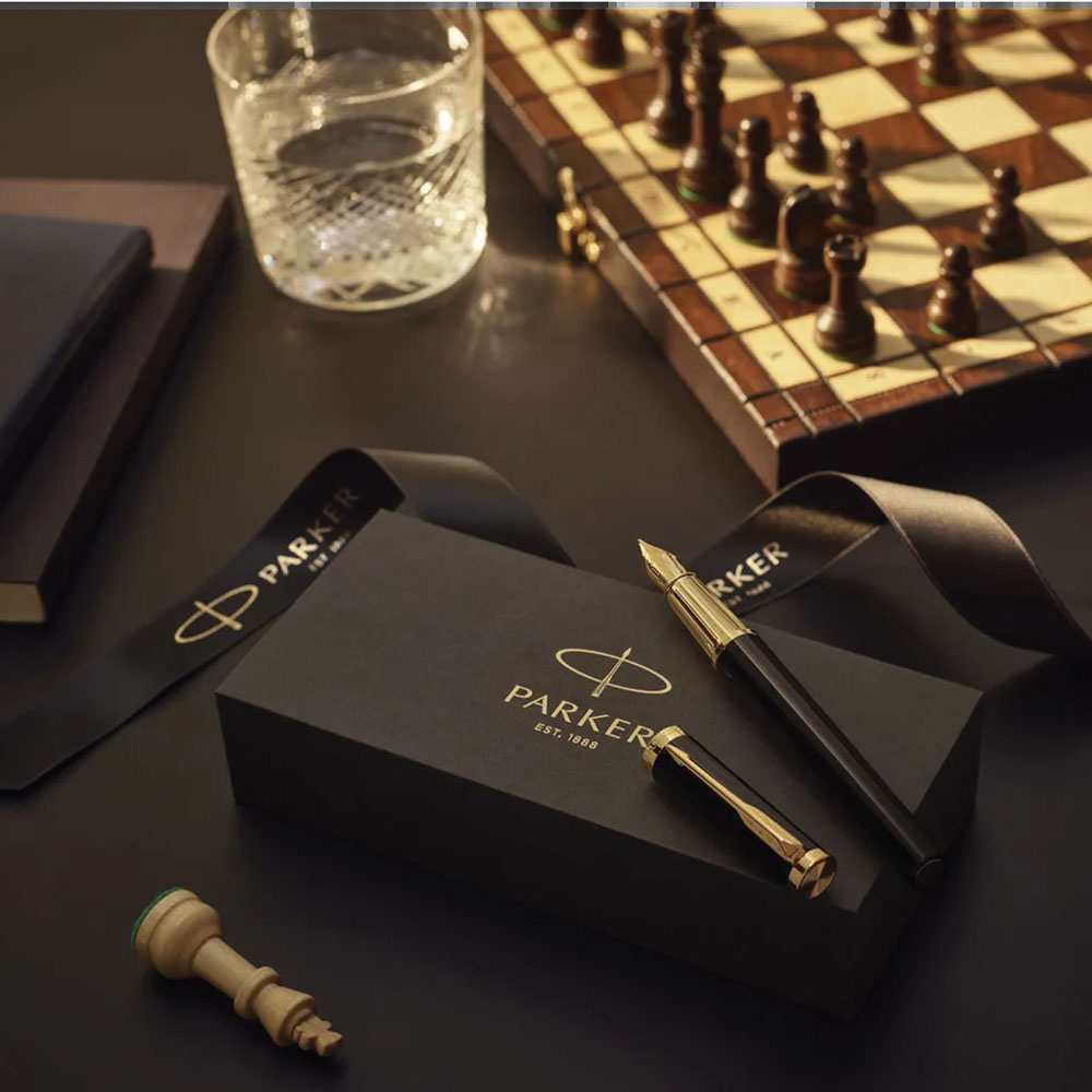 Pióro Parker na eleganckim pudełku prezentowym obok szachownicy i szklanki whisky.